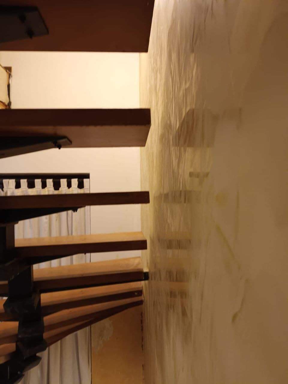 Hohe Treppenhauswand in heller Spachteltechnik neben einer Holztreppe.