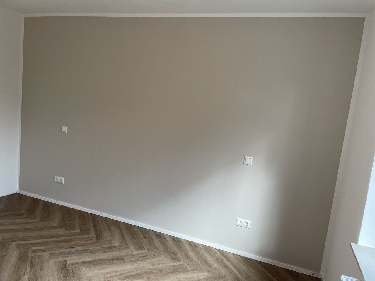 Wohnraumwand in warmem Greige, über die das Tageslicht von rechts nach links immer dunkler verläuft.