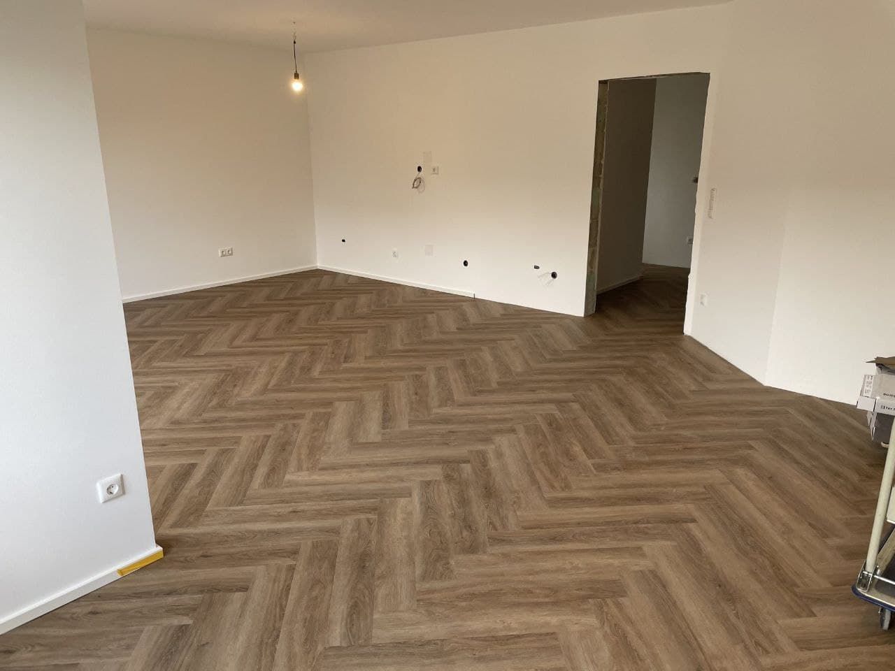 Leerer Wohnraum mit hell gestrichenen Wänden und neu verlegtem Fischgrätboden.